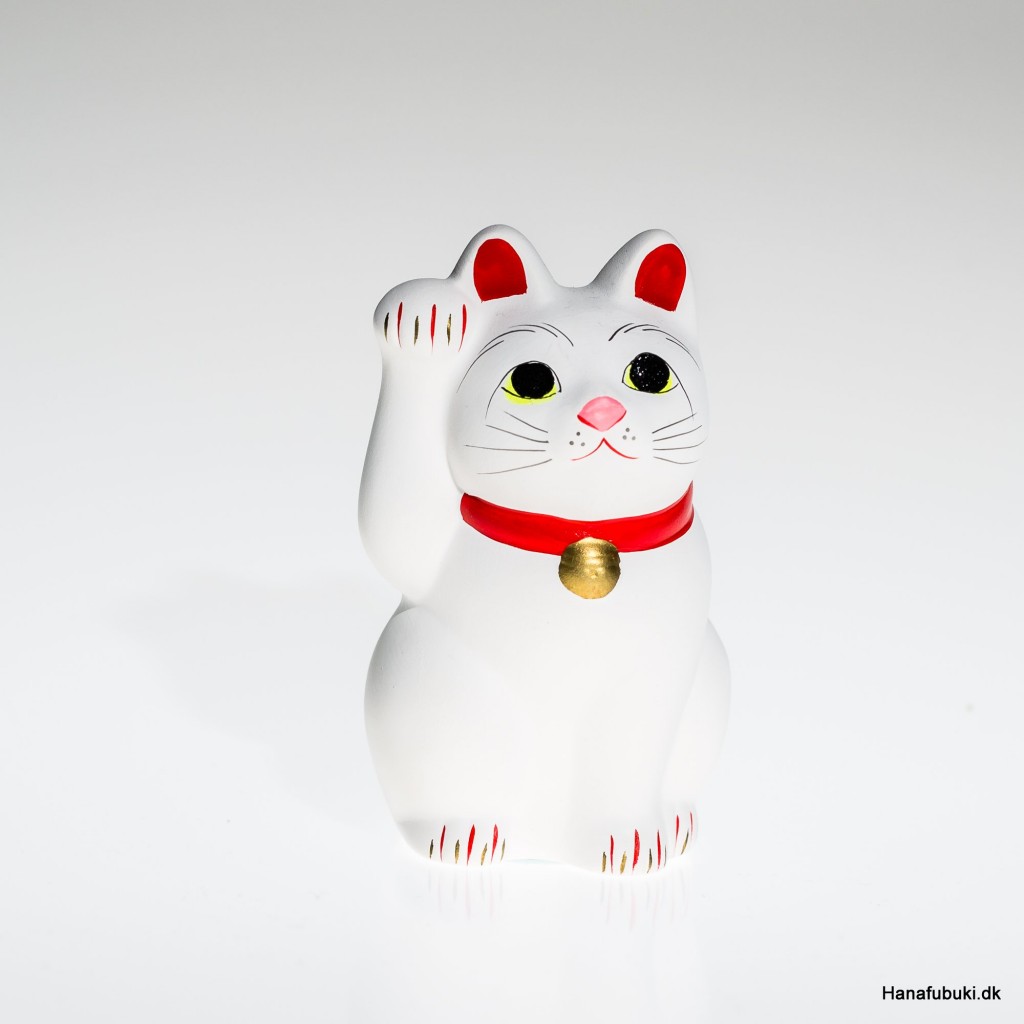 Hvid maneki neko med rødt halsbånd og løftet pote